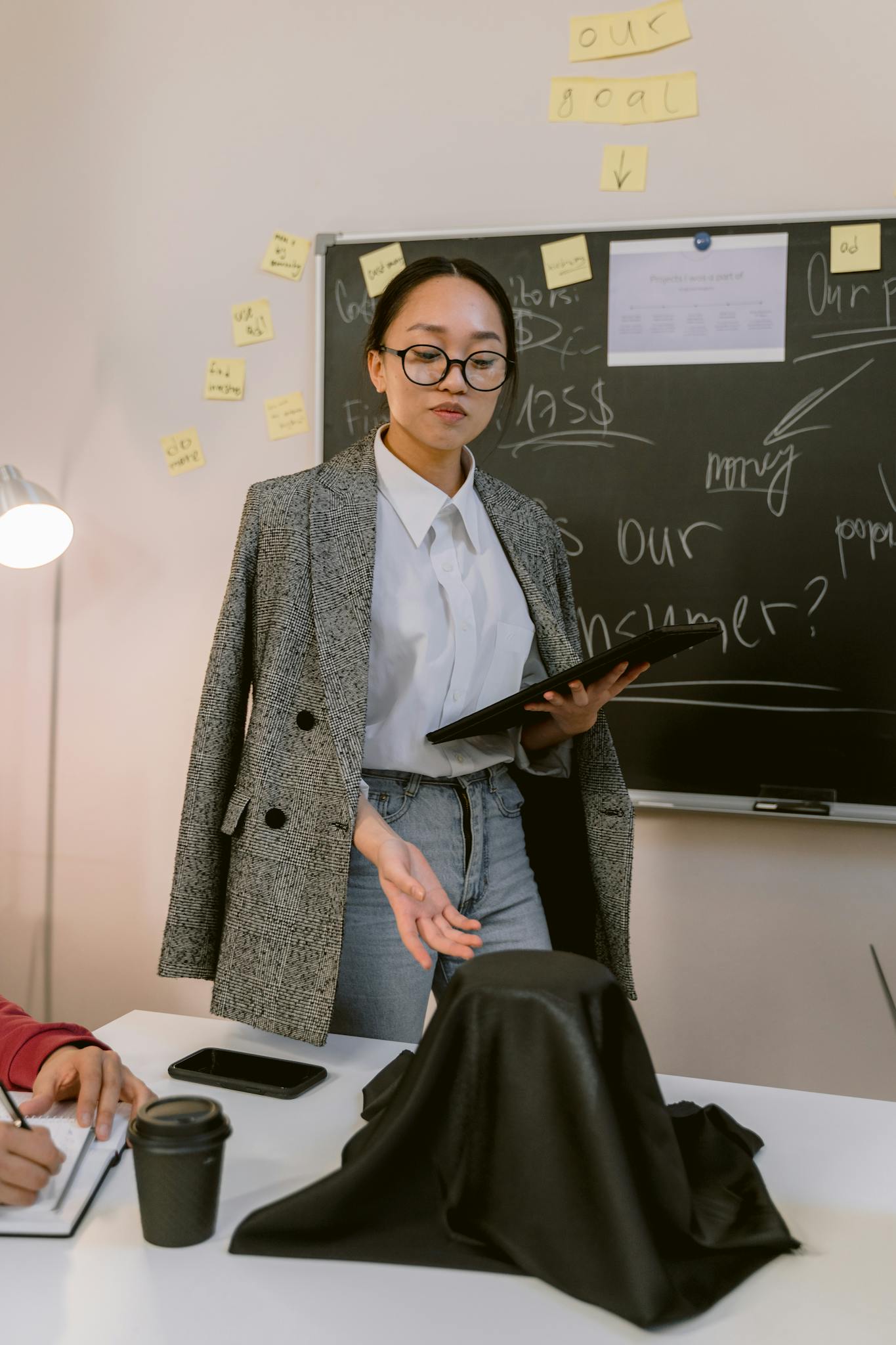 Asian woman in a blazer presenting during a business meeting indoors.